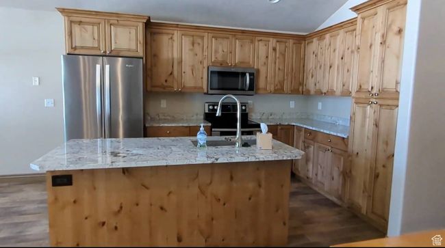 Kitchen with appliances with stainless steel finishes, wood finished floors, a sink, a center island with sink, and vaulted ceiling | Image 8