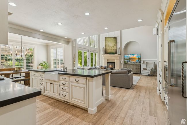 Kitchen featuring cream cabinets, dark countertops, a glass covered fireplace, light wood finished floors, and a chandelier | Image 16