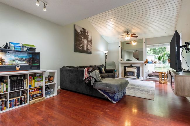 Living area featuring a glass covered fireplace, ceiling fan, wood finished floors, and lofted ceiling | Image 5