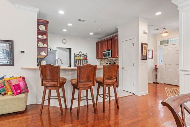 Kitchen featuring ornamental molding, stainless steel microwave, light countertops, a peninsula, and a kitchen bar | Image 25