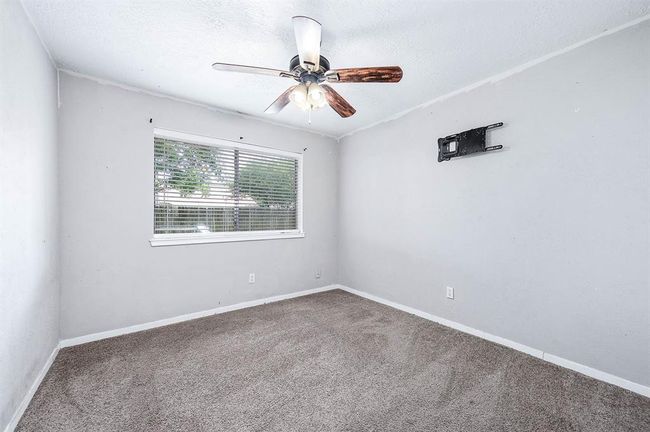 This bedroom features neutral walls, a carpeted floor, a ceiling fan with lights, and a window that allows natural light. There is a wall mount for a TV. | Image 14