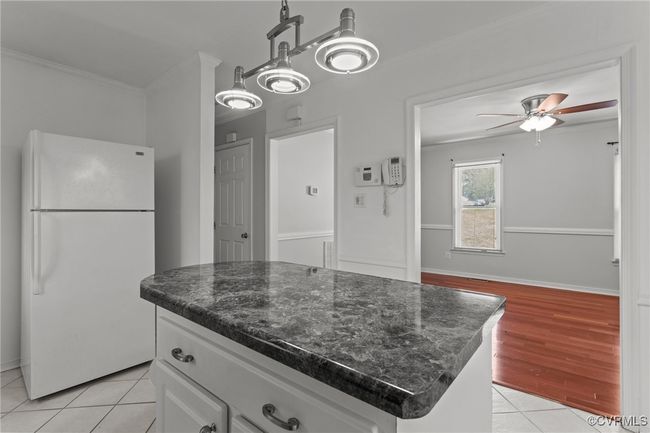 Kitchen with white cabinets, a ceiling fan, freestanding refrigerator, crown molding, and dark stone counters | Image 13