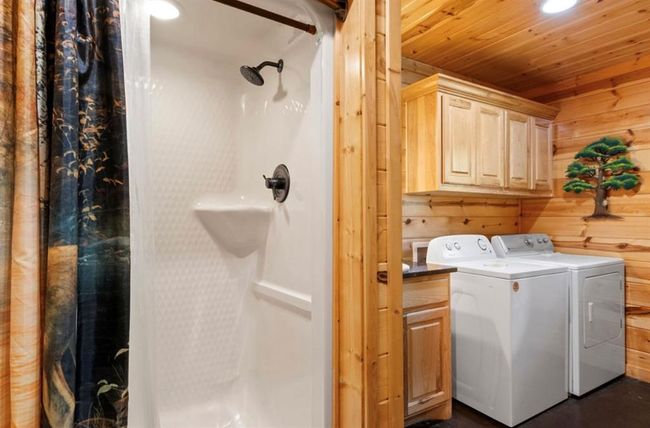 Laundry area featuring independent washer and dryer, wood walls, cabinet space, and wood ceiling | Image 22