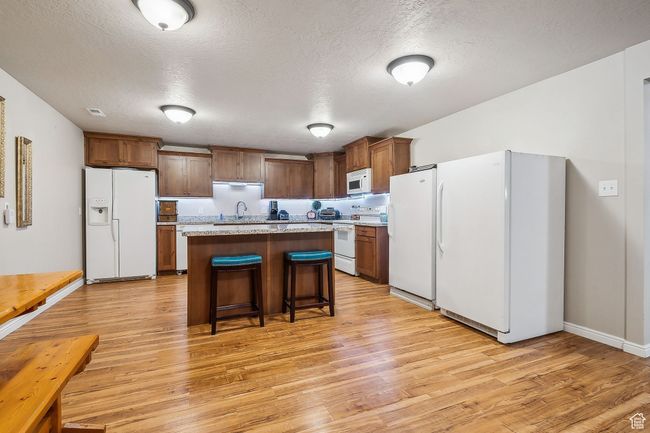 Kitchen with light wood finished floors, a breakfast bar, white appliances, and a kitchen island | Image 45