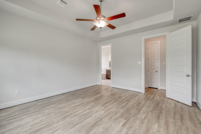 Unfurnished bedroom with a raised ceiling, light wood finished floors, ensuite bath, and ceiling fan | Image 17