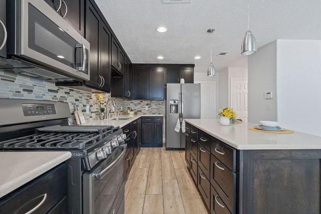 Kitchen with appliances with stainless steel finishes, light wood-type flooring, light countertops, decorative backsplash, and recessed lighting | Image 25