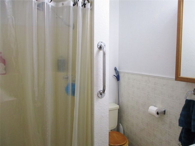 Full bathroom with toilet, a shower with curtain, tile walls, and a wainscoted wall | Image 16