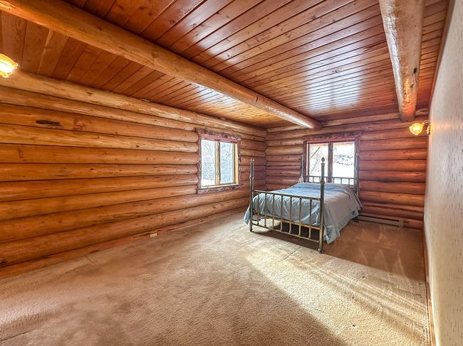 Unfurnished bedroom with beam ceiling, rustic walls, and multiple windows | Image 38