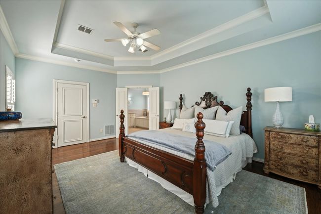 Bedroom featuring a raised ceiling, ornamental molding, wood finished floors, a ceiling fan, and ensuite bathroom | Image 23