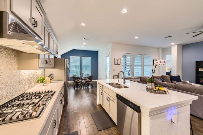 Kitchen featuring under cabinet range hood, stainless steel appliances, open floor plan, an island with sink, and light countertops | Image 12