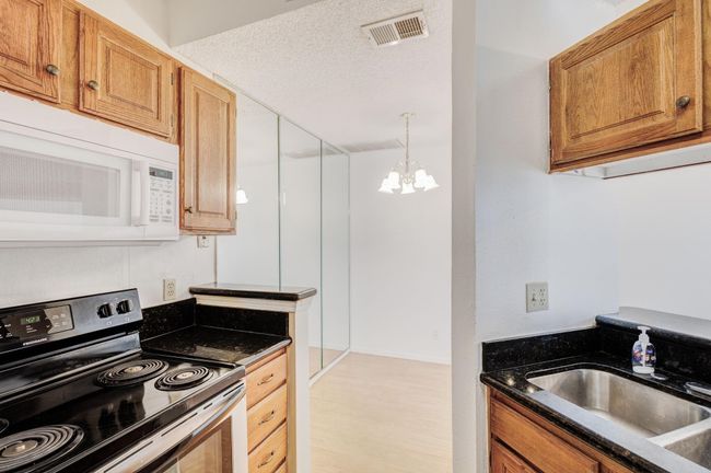 Kitchen featuring electric stove, white microwave, a sink, a chandelier, and brown cabinetry | Image 5