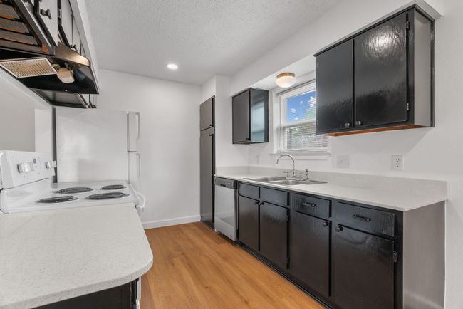 Kitchen with white appliances, light wood-style floors, a textured ceiling, light countertops, and range hood | Image 15