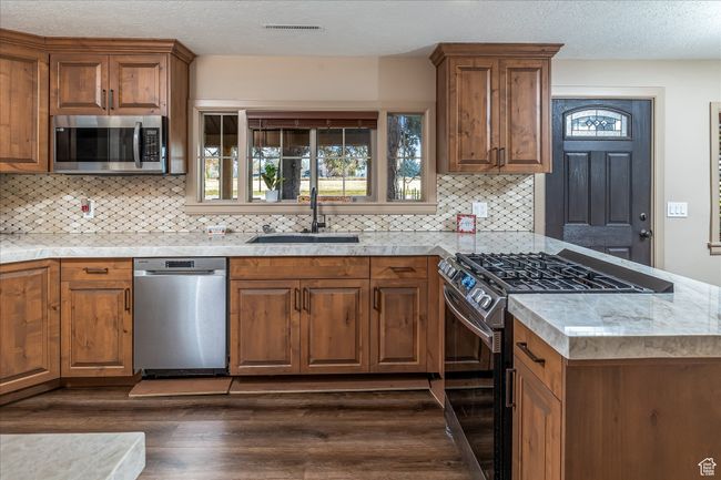 Kitchen featuring stainless steel appliances, dark wood-type flooring, brown cabinetry, decorative backsplash, and a peninsula | Image 17