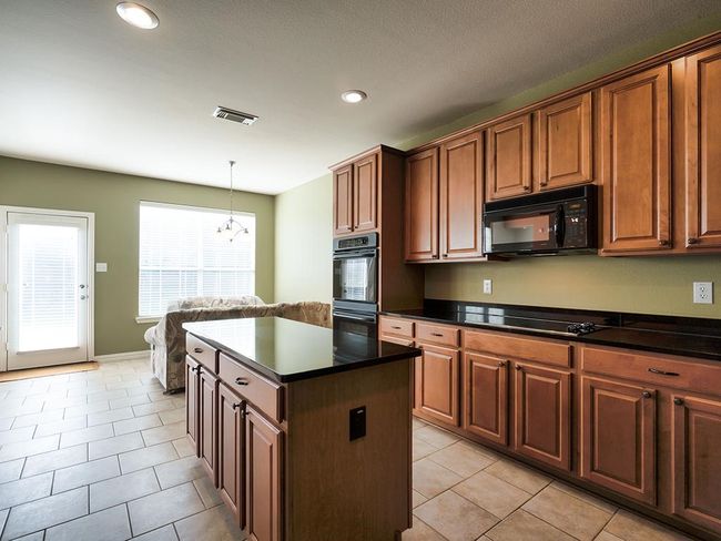 Kitchen with black appliances, dark countertops, a kitchen island, light tile patterned floors, and recessed lighting | Image 16