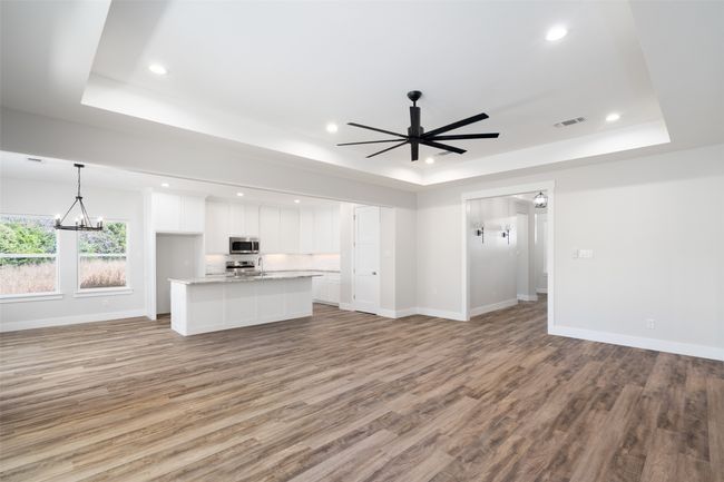 Unfurnished living room with a raised ceiling, light hardwood / wood-style floors, and ceiling fan with notable chandelier | Image 12