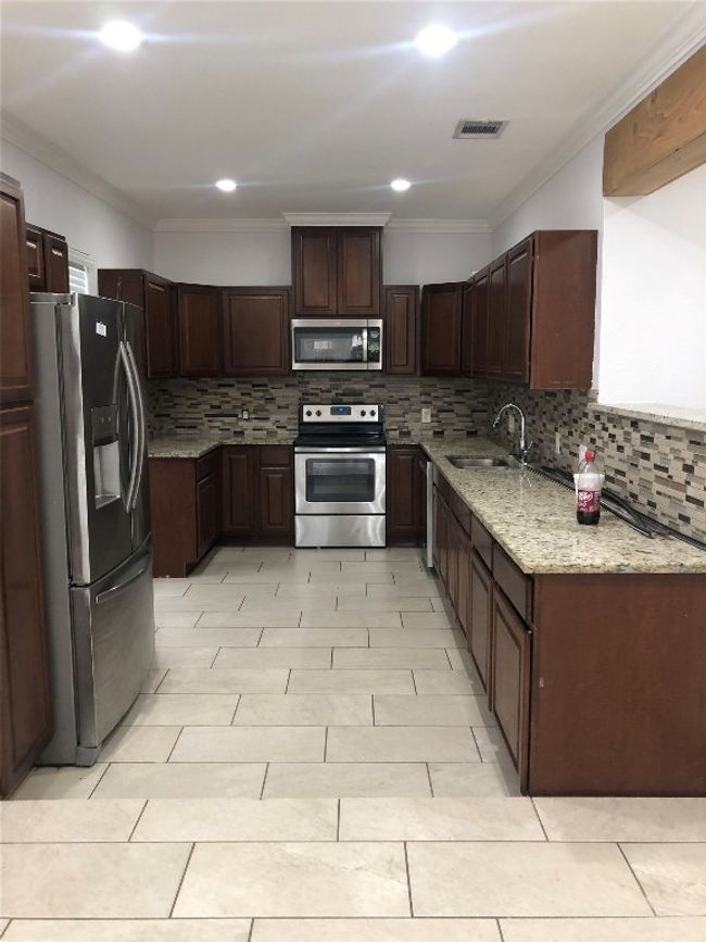 Kitchen with stainless steel appliances, decorative backsplash, light stone counters, ornamental molding, and dark brown cabinets | Image 9