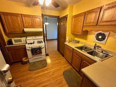 Kitchen with white appliances, light wood-type flooring, ceiling fan, decorative light fixtures, and sink | Image 3