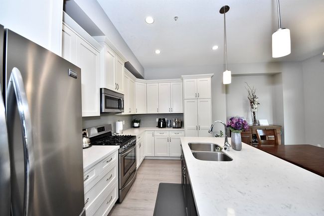 Kitchen with stainless steel appliances, a sink, recessed lighting, white cabinets, and hanging light fixtures | Image 5