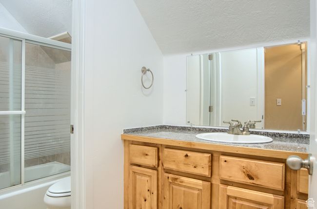 Bathroom with lofted ceiling, toilet, vanity, bath / shower combo with glass door, and a textured ceiling | Image 19