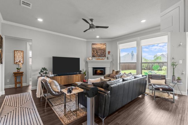 Living room with a ceiling fan, a lit fireplace, dark wood finished floors, recessed lighting, and crown molding | Image 11