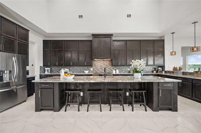 This is a spacious modern kitchen featuring stainless steel appliances, a large 15 foot central island with seating, and elegant granite countertops complemented by a stylish backsplash. The room is well-lit with natural light. | Image 3