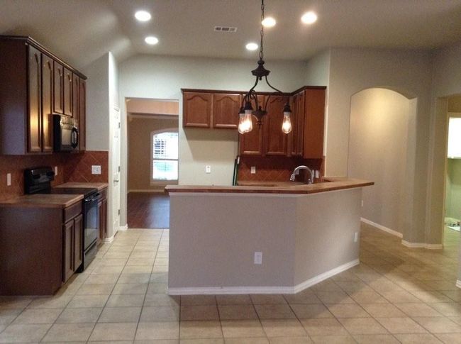 Kitchen featuring light tile patterned floors, tasteful backsplash, visible vents, arched walkways, and black appliances | Image 5
