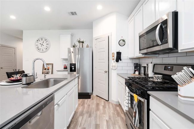 Stylish kitchen boasts quartz countertops, stainless steel appliances, white cabinetry, and a pass-through bar for easy entertaining. | Image 8