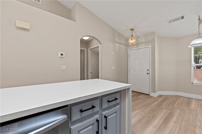 Kitchen featuring stainless steel dishwasher, light wood-type flooring, gray cabinetry, arched walkways, and light stone countertops | Image 12