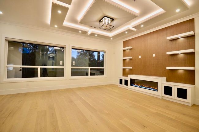 Unfurnished living room with wood finished floors, a chandelier, ornamental molding, a glass covered fireplace, and recessed lighting | Image 7