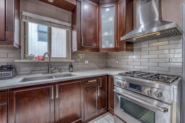 Kitchen featuring wall chimney range hood, high end stove, backsplash, and glass insert cabinets | Image 10