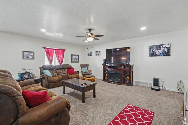 Carpeted living room featuring visible vents, baseboards, a ceiling fan, a textured ceiling, and a fireplace | Image 10
