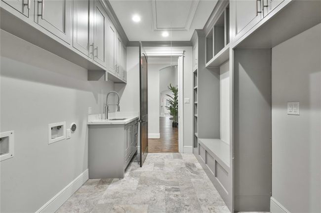 This spacious laundry room is thoughtfully designed for maximum functionality and convenience. It features hookups for two washers and two dryers, making it ideal for large households. A sizable countertop provides plenty of workspace for folding, sorting, and organizing laundry tasks. | Image 21