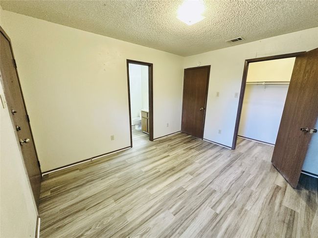 Unfurnished bedroom with light wood-type flooring, a textured ceiling, a closet, and ensuite bathroom | Image 18