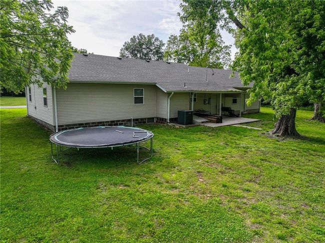 Rear view of house with a trampoline, a patio, central AC, and a lawn | Image 6