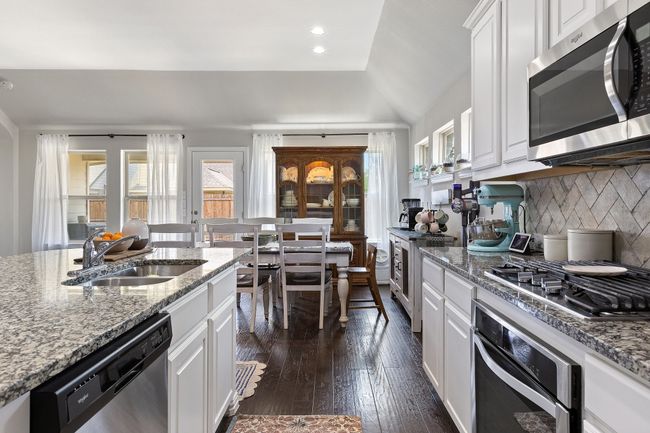 Kitchen featuring white cabinets, a sink, dark wood finished floors, decorative backsplash, and appliances with stainless steel finishes | Image 11