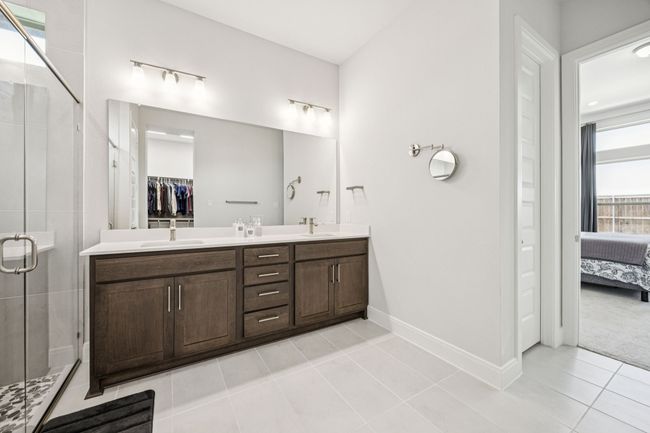 Ensuite bathroom featuring double vanity, tile patterned floors, a stall shower, baseboards, and a walk in closet | Image 17