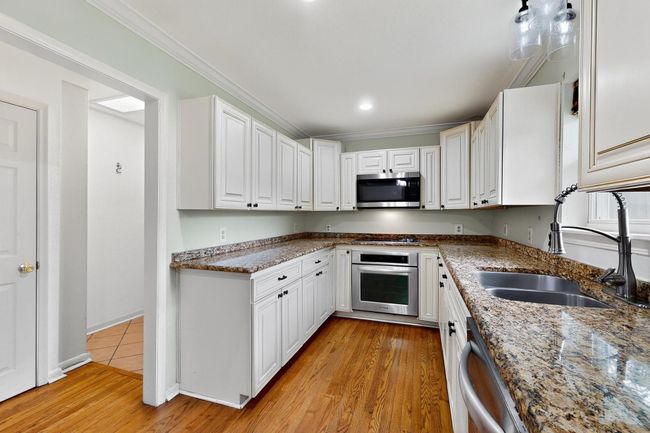 Kitchen with appliances with stainless steel finishes, white cabinetry, crown molding, stone counters, and light wood-style floors | Image 8