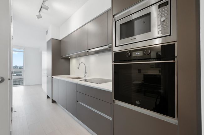 Kitchen with gray cabinets, light countertops, black appliances, modern cabinets, and a sink | Image 6