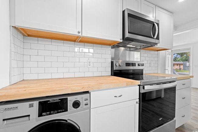 Kitchen featuring washer / clothes dryer, appliances with stainless steel finishes, wood counters, white cabinets, and backsplash | Image 9