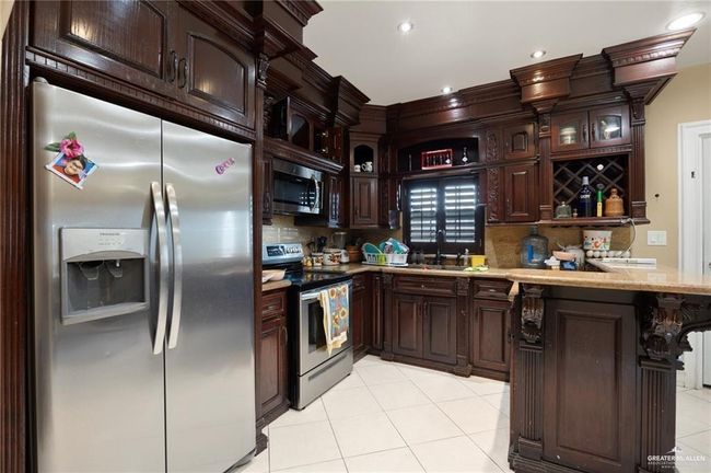 Kitchen featuring sink, dark brown cabinetry, light tile patterned floors, appliances with stainless steel finishes, and kitchen peninsula | Image 5