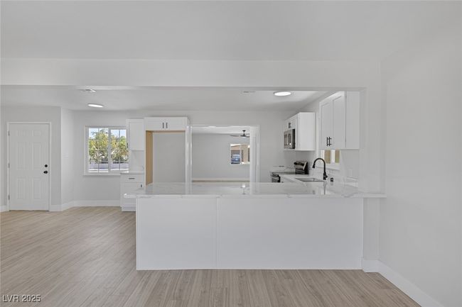 Kitchen featuring stainless steel appliances, white cabinets, light wood-type flooring, a peninsula, and light stone countertops | Image 8