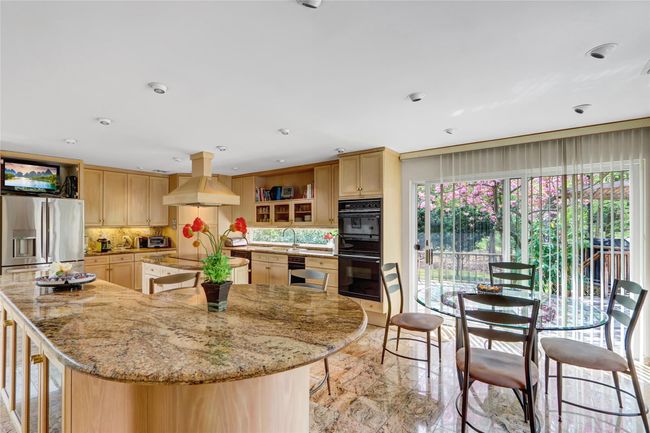 Kitchen featuring island range hood, a spacious island, light brown cabinetry, open shelves, and black appliances | Image 8
