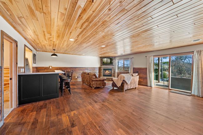 Lower level grand family room with T&G ceiling, reclaimed wood walls, heated floors, walkout, gas fireplace, and wet bar! | Image 24