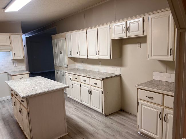 Kitchen featuring backsplash, light wood-style flooring, under cabinet range hood, and white cabinetry | Image 11