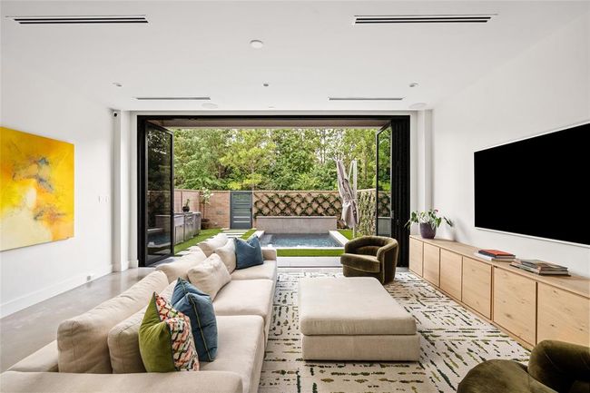 This stunning living room offers a seamless blend of indoor-outdoor living, featuring floor-to-ceiling sliding glass doors that open onto a private pool and lush greenery. Designed for comfort and style, the space features polished concrete floors and a cozy lounge area. Perfect for entertaining or relaxing, this space combines natural light, clean lines, and modern warmth to create a truly inviting setting. | Image 5