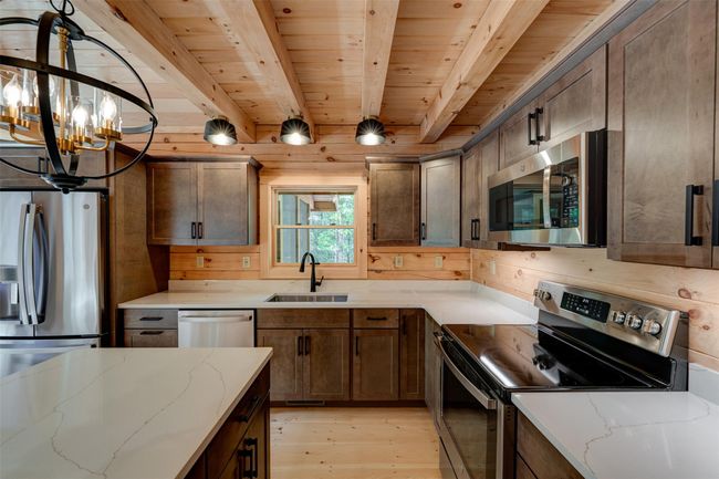 Kitchen with stainless steel appliances, light wood-style flooring, a sink, wooden ceiling with exposed beams, and a chandelier | Image 13