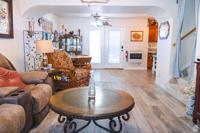 Living area with arched walkways, heating unit, a ceiling fan, light wood finished floors, and stairway | Image 8