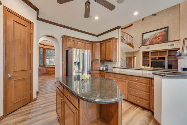 Kitchen featuring stainless steel fridge, a ceiling fan, light wood-style floors, a center island, and dark stone countertops | Image 8