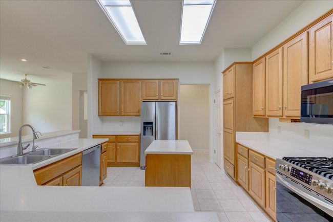 Kitchen with stainless steel finishes, a kitchen island, light tile patterned floors, & light countertops | Image 12