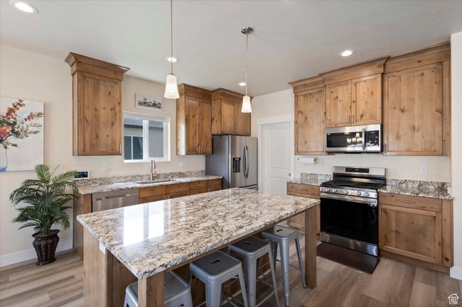 Kitchen featuring stainless steel appliances, light wood-type flooring, a breakfast bar, light stone counters, and recessed lighting | Image 9